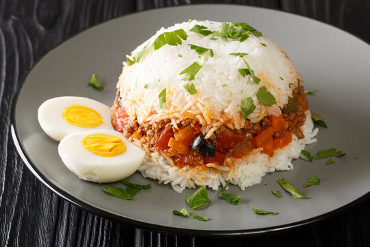 Tasty Arroz tapado is a Peruvian dish consisting with rice, vegetables, ground beef and boiled eggs close up in the plate on the table. Horizontal