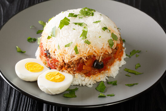 Arroz tapado is a Peruvian dish it is made with rice, vegetables, ground beef and boiled eggs close up in the plate on the table. Horizontal