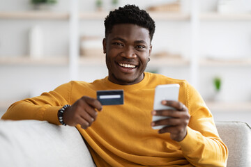 Happy young black man using cellphone and holding credit card