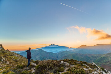 Man standing on top of the cliff in the mountains at sunset enjoying the beautiful sunset over...
