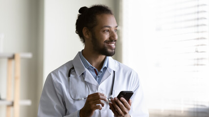 Smiling young African American man doctor wearing white uniform with stethoscope holding...