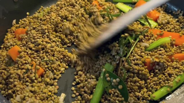 Italian home made winter food. Cooking Italian Christmas delicacies at home. Raw lentils frying in a pan with a rosemary, carrot, celery and onion soffritto, stirred around with a wooden spoon.