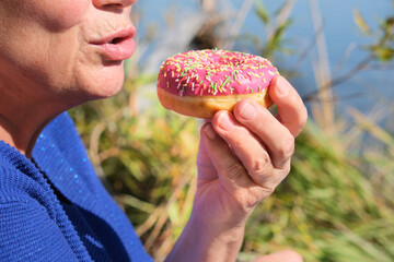Senior woman holding delicious pink doughnut. Picnic