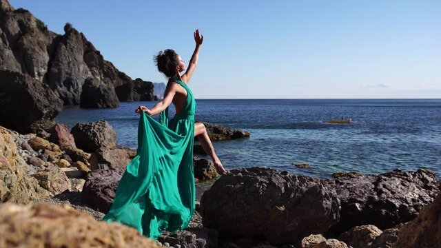 Side view a Young beautiful sensual woman with black hair in a long mint dress posing on a beach with calm sea bokeh lights on sunny day. Girl on the nature on blue sky background. Fashion photo