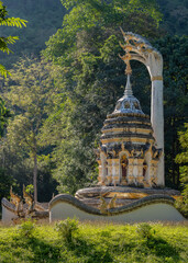 White and golden stupa protected by mucalinda naga with tropical forest in background on the slopes of Doi Luang mountain, Wat Tham Chiang Dao cave buddhist temple, Chiang Dao, Chiang Mai, Thailand