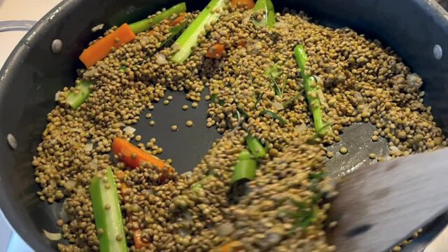 Cooking Italian Christmas delicacies at home. Raw lentils frying in a pan with a rosemary, carrot, celery and onion soffritto, stirred around with a wooden spoon. Mouth watering.