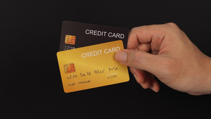 Hand is holding or showing two credit cards in black and gold color isolated on black background.