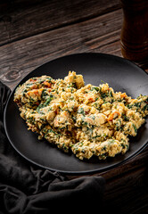 scrambled eggs with spinach and tomato in plate on wooden table background