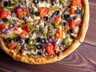 Close-up of a delicious vegetarian pizza with vegetables and mushrooms on a brown wooden background. Top view, flat lay. Unhealthy food.