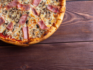 Close-up pizza with ham and mushrooms on a brown wooden background. A traditional Italian dish. A delicious and unhealthy dish. Top view, flat lay, copy space