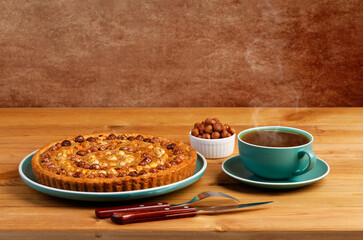 Homemade pie decorated with nuts hazelnut and a cup of tea on a wooden table. Copyspace.