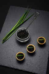 Fototapeta na wymiar natural sturgeon black caviar in a glass jar on a slate plate and tartlets close-up - a national dish of Russian cuisine