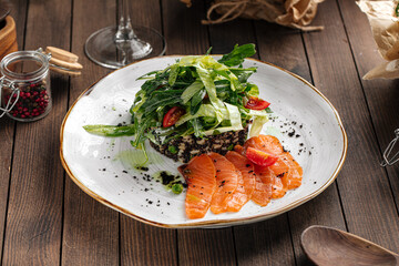 Plate of salted sliced salmon and green salad on wooden background