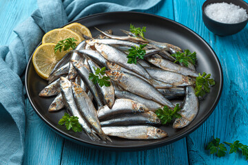 A dish with salted sprat with lemon and parsley on a blue background. - obrazy, fototapety, plakaty