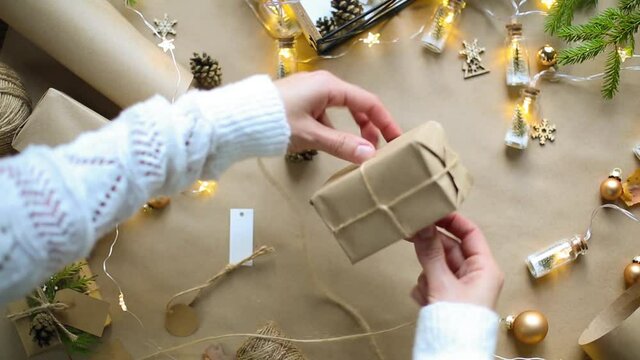 Hands pack a gift for Christmas and new year in eco-friendly materials: kraft paper, live fir branches, cones, twine, tied with a bow. Tags with mock up, natural decor, hand made, flatly. Festive mood