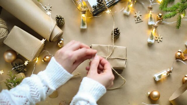 Hands pack a gift for Christmas and new year in eco-friendly materials: kraft paper, live fir branches, cones, twine, tied with a bow. Tags with mock up, natural decor, hand made, flatly. Festive mood