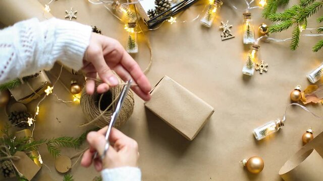 Hands pack a gift for Christmas and new year in eco-friendly materials: kraft paper, live fir branches, cones, twine, tied with a bow. Tags with mock up, natural decor, hand made, flatly. Festive mood