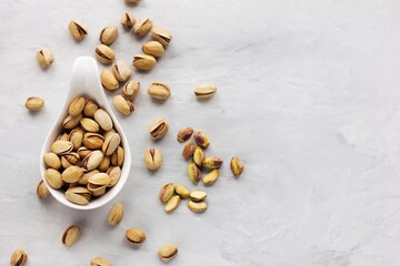 A white plate with rav pistachios in a shell shell on a grey background