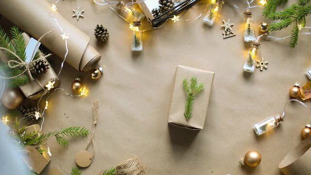 Hands pack a gift for Christmas and new year in eco-friendly materials: kraft paper, live fir branches, cones, twine, tied with a bow. Tags with mock up, natural decor, hand made, flatly. Festive mood