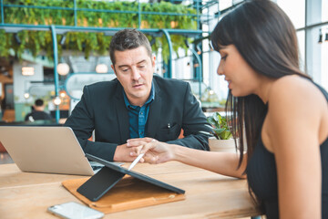 business partners have fun using smartphone together, with laptop computer at coffee shop. Information technology, cafe lifestyle.