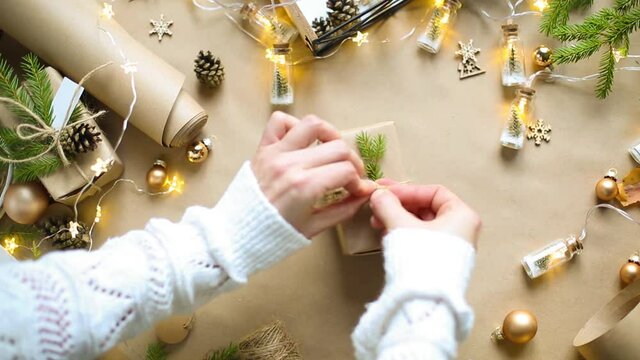 Hands pack a gift for Christmas and new year in eco-friendly materials: kraft paper, live fir branches, cones, twine, tied with a bow. Tags with mock up, natural decor, hand made, flatly. Festive mood