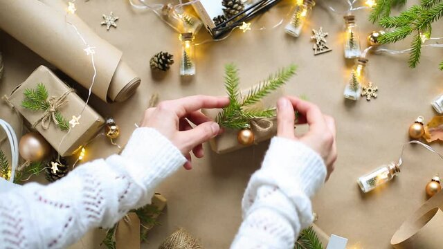 Hands pack a gift for Christmas and new year in eco-friendly materials: kraft paper, live fir branches, cones, twine, tied with a bow. Tags with mock up, natural decor, hand made, flatly. Festive mood