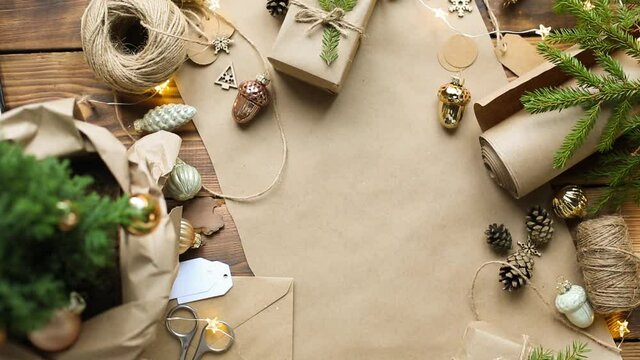 Hands pack a gift for Christmas and new year in eco-friendly materials: kraft paper, live fir branches, cones, twine, tied with a bow. Tags with mock up, natural decor, hand made, flatly. Festive mood