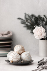 Preparing for a festive table setting, a stack of different plates and forks with knives, fir branches in a concrete vase, Christmas balls and decorations
