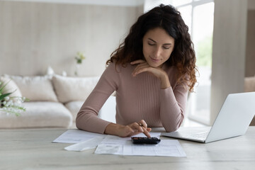 Young woman using calculator and laptop, calculating finances or taxes, sitting at work desk at home, female managing budget, household expenses, paying bills on computer, internet banking service - obrazy, fototapety, plakaty