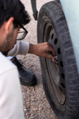vertical image of a young man changing the flat tire of a car after an accident