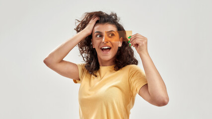 Fototapeta premium Excited woman holding orange film in front of her eyes, looking aside, posing isolated over light background