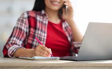 Home Office. Closeup Of Young Woman Talking On Cellphone And Taking Notes