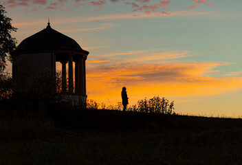 Alone in the early morning in nature: silhouette of a man in the sunrise with landscape and an ancient building