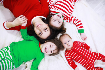 A family in striped pajamas is resting at home. Little children dressed as elves are lying on the sofa. Happy family.