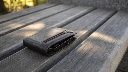A leather money wallet left on a park bench. Lost thing. - obrazy, fototapety, plakaty