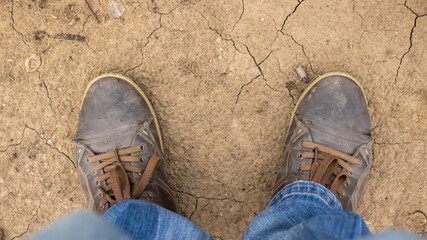 The legs of the photographer. Old shoes and jeans. Cracked dry earth.