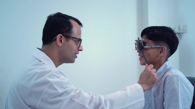 Boy doing eye test checking examination with optometrist in optical shop, Smiling Indian-thai boy choosing glasses in optics store