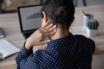 Rear back shoulder view stressed young Indian ethnicity woman massaging neck, suffering from severe...