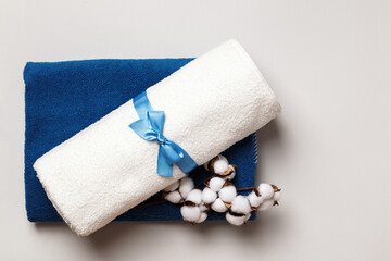 Rolled up white and blue terry towels with a cotton twig on a gray background.