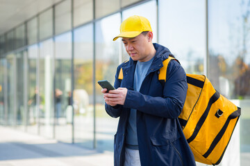 Happy male courier walking food supplier, looking forward to new order received in phone app, asian courier
