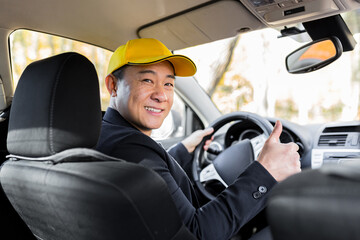 Male courier asian looks into the camera and smiles holding a parcel sitting in the car