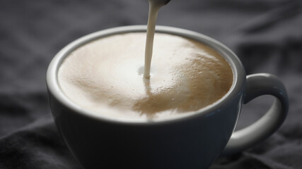 pour steamed milk into white cup making cappuccino