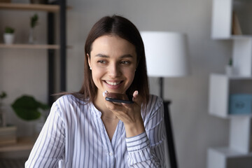 Smiling young business lady holding distant loudspeaker conversation, recoding audio message on...
