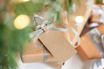 Holiday gift box. Christmas present with address card tag under fir tree on floor in room....
