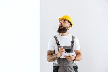 An electrician with a helmet on his head is standing in the freshly painted room, writing down what...