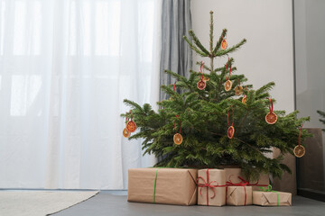 Fototapeta na wymiar Small christmas tree with gifts in paper wrap near window