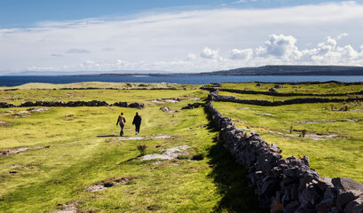 Beautiful landscape scenery of green field and stone wall with people passing by at Aran islands in County Galway, Ireland 