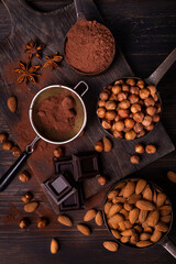 Still life. in the foreground with top view, vintage metal measuring spoons with shelled hazelnuts and almonds, cocoa powder, pieces of dark chocolate and star anise stars - obrazy, fototapety, plakaty