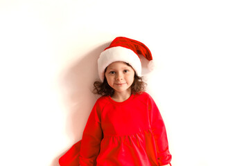 Cute little girl in a red Christmas hat and red dress on a red background. Merry Christmas and Happy Holidays.