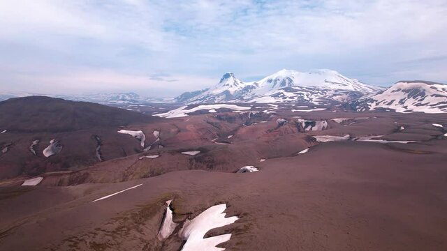 Sideways moving aerial shot of mountainous landscape in Iceland. Road in the distance and snowy mountains. 